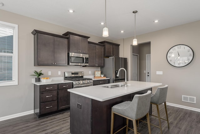 kitchen with dark brown cabinets, appliances with stainless steel finishes, an island with sink, and hanging light fixtures