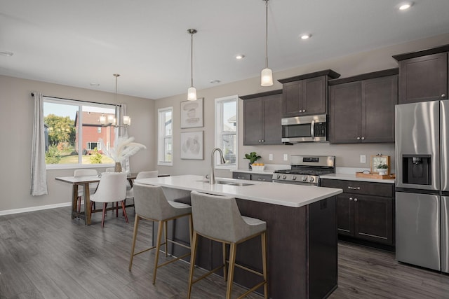 kitchen with sink, hanging light fixtures, dark brown cabinetry, stainless steel appliances, and a center island with sink