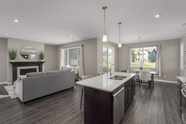 kitchen featuring sink, a kitchen island with sink, hanging light fixtures, a stone fireplace, and stainless steel dishwasher