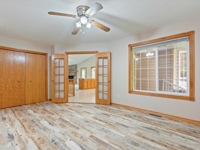 unfurnished bedroom featuring a fireplace, a textured ceiling, french doors, a closet, and light wood-type flooring