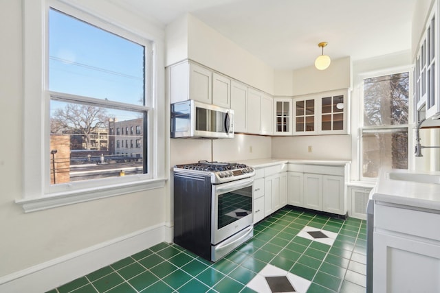 kitchen featuring stainless steel appliances, a sink, white cabinets, light countertops, and glass insert cabinets