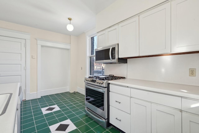 kitchen with dark tile patterned flooring, white cabinetry, baseboards, light countertops, and appliances with stainless steel finishes