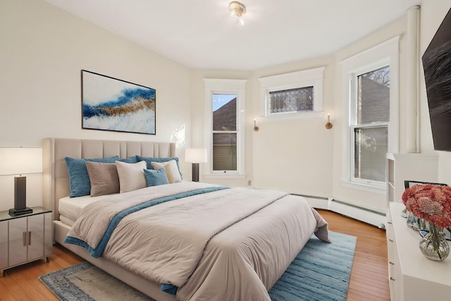 bedroom with multiple windows, baseboard heating, and light wood-style flooring