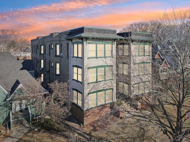 view of home's exterior with a shingled roof, mansard roof, and stucco siding