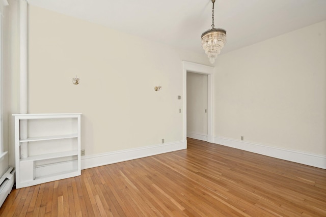 spare room with baseboard heating, an inviting chandelier, hardwood / wood-style flooring, and baseboards