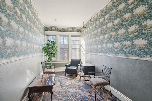 sitting room with crown molding, wainscoting, baseboards, and wallpapered walls