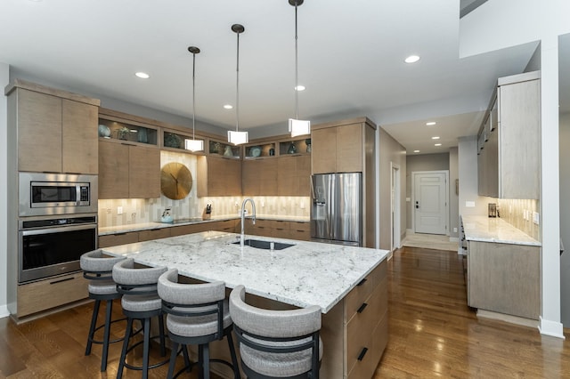 kitchen with tasteful backsplash, a sink, a center island with sink, appliances with stainless steel finishes, and dark wood-style flooring