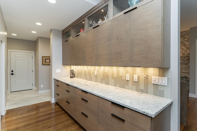 kitchen with light stone counters, dark wood finished floors, recessed lighting, glass insert cabinets, and modern cabinets