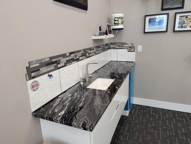 kitchen with dark stone counters, baseboards, and a sink