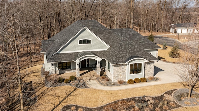 view of front facade featuring covered porch, stone siding, driveway, and a shingled roof