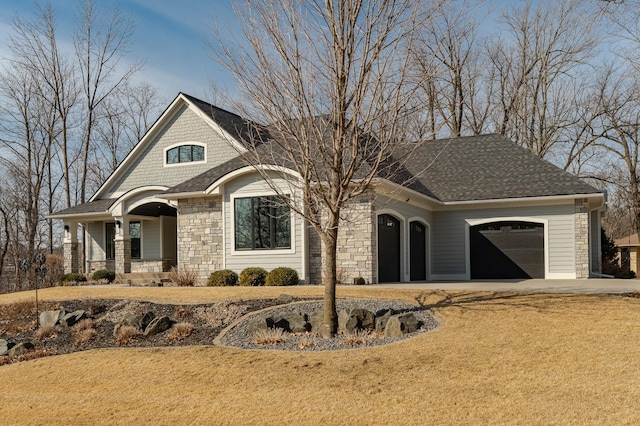 view of front facade with driveway, roof with shingles, an attached garage, covered porch, and stone siding