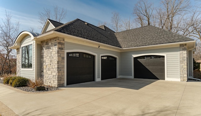 view of side of property featuring stone siding, driveway, an attached garage, and roof with shingles