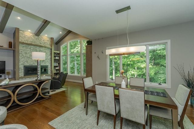 dining space featuring wood finished floors, baseboards, vaulted ceiling with beams, recessed lighting, and a stone fireplace