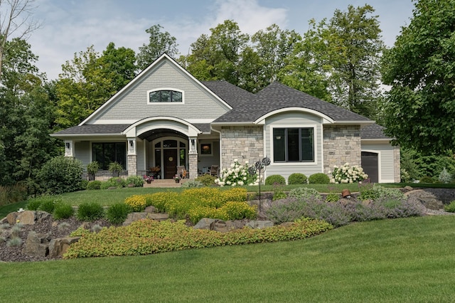 view of front of home with a front lawn, stone siding, a porch, a shingled roof, and a garage