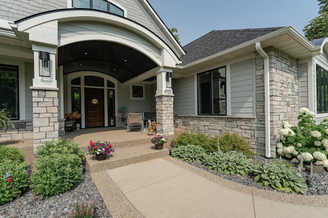 property entrance with stone siding, a porch, and a shingled roof