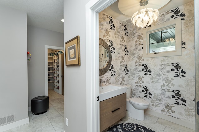 bathroom with wallpapered walls, a chandelier, toilet, vanity, and a walk in closet