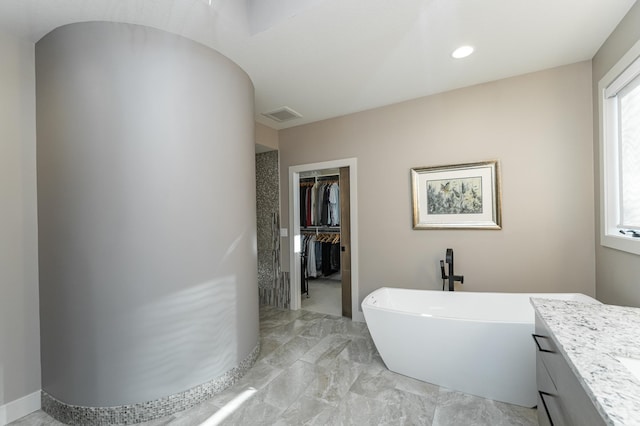 bathroom with a freestanding bath, a walk in closet, gas water heater, marble finish floors, and vanity