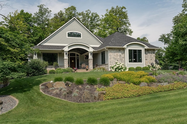 view of front facade featuring stone siding, a front lawn, a porch, and a shingled roof