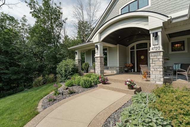 view of exterior entry with covered porch, a lawn, and stone siding