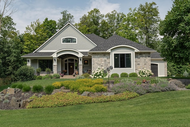 view of front of home with stone siding, a porch, a front yard, and a garage