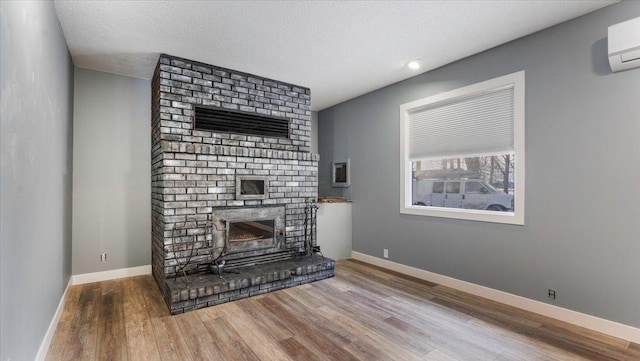 unfurnished living room with a wall mounted air conditioner, hardwood / wood-style floors, a brick fireplace, and a textured ceiling