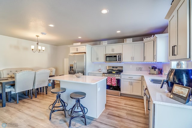 kitchen with white cabinets, hanging light fixtures, a center island, stainless steel appliances, and light wood-type flooring