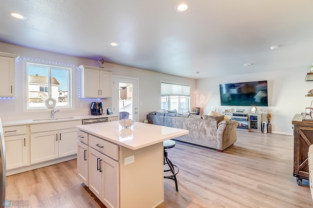 kitchen with a kitchen island, sink, white cabinets, a kitchen breakfast bar, and light hardwood / wood-style floors