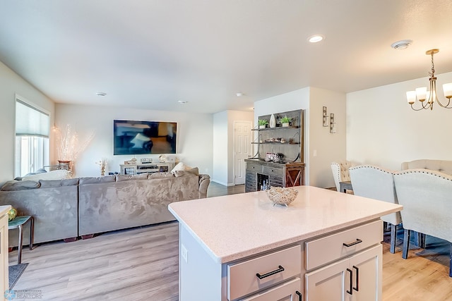 kitchen with a kitchen island, white cabinets, hanging light fixtures, light hardwood / wood-style floors, and an inviting chandelier