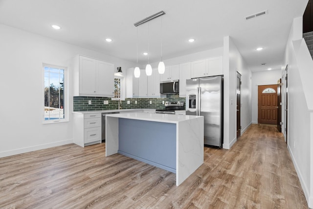 kitchen featuring stainless steel appliances, light hardwood / wood-style floors, white cabinets, a kitchen island, and decorative light fixtures