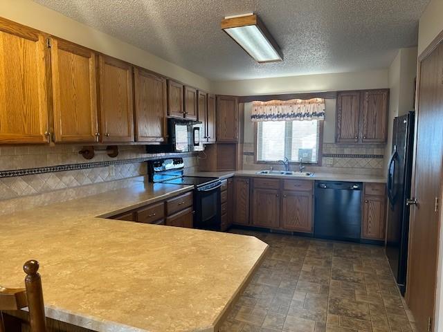 kitchen featuring sink, black appliances, a textured ceiling, decorative backsplash, and kitchen peninsula