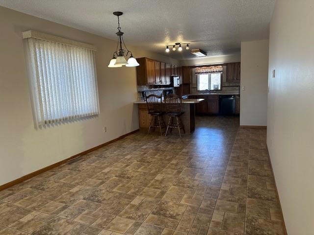 kitchen with a breakfast bar, a textured ceiling, appliances with stainless steel finishes, kitchen peninsula, and pendant lighting