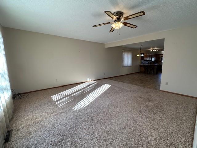 unfurnished living room with ceiling fan, plenty of natural light, carpet flooring, and a textured ceiling