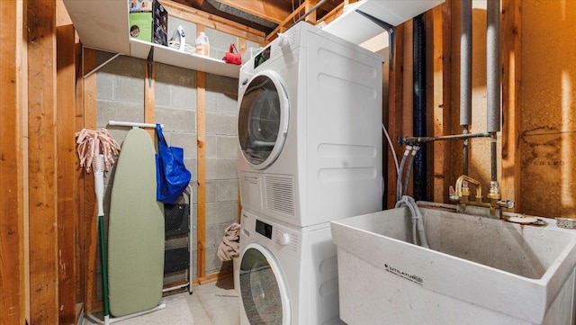 washroom with laundry area, concrete block wall, stacked washer / drying machine, and a sink