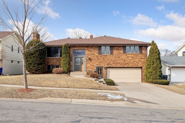 bi-level home featuring brick siding, roof with shingles, a chimney, concrete driveway, and an attached garage