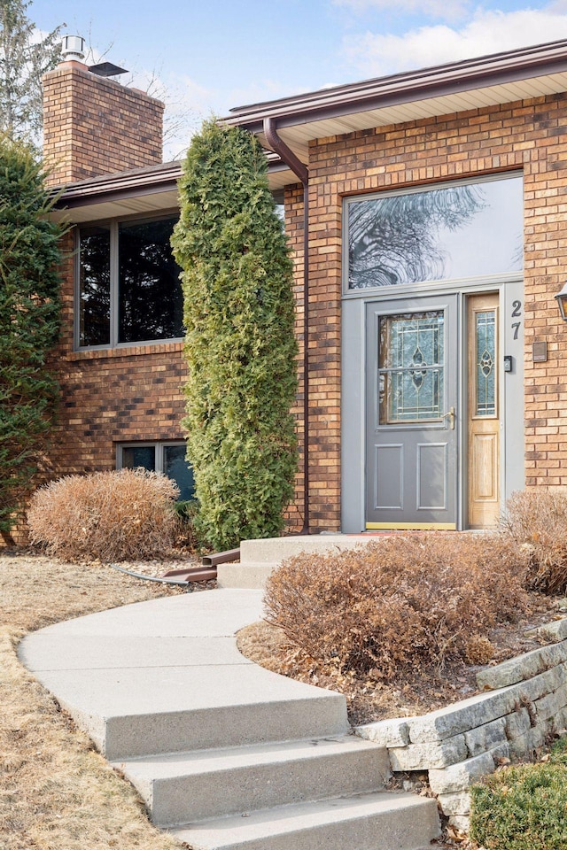 view of exterior entry with brick siding and a chimney