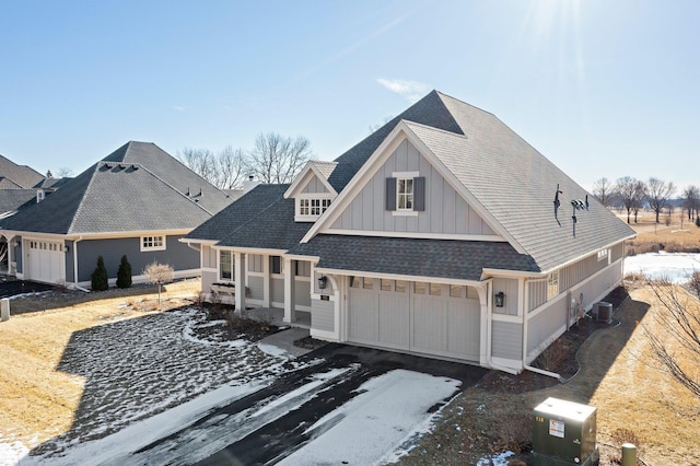 view of front facade featuring a garage, central AC unit, aphalt driveway, roof with shingles, and board and batten siding