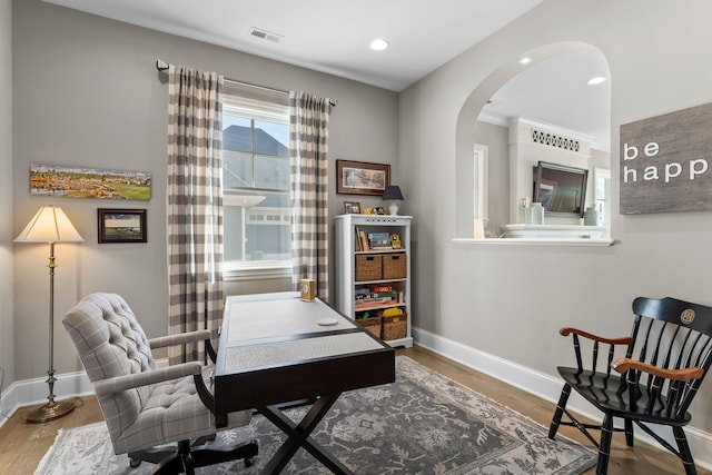 office space with baseboards, visible vents, arched walkways, and wood finished floors