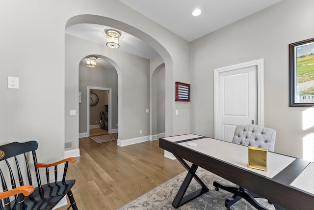 office area with arched walkways, wood finished floors, visible vents, baseboards, and washer / clothes dryer