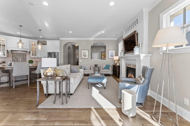 living area featuring ornamental molding, a glass covered fireplace, arched walkways, and wood finished floors