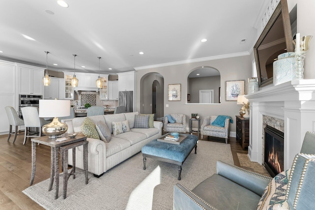 living room with arched walkways, recessed lighting, a fireplace, light wood-style floors, and crown molding