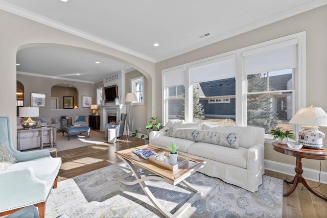 living room featuring a warm lit fireplace, visible vents, wood finished floors, crown molding, and recessed lighting