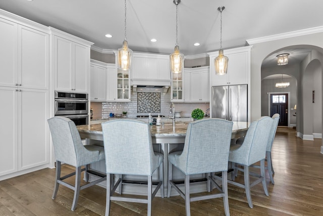 kitchen featuring tasteful backsplash, arched walkways, dark wood finished floors, glass insert cabinets, and stainless steel appliances