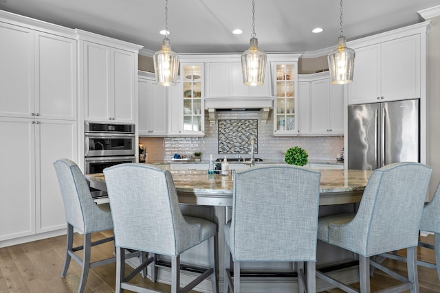 kitchen with stainless steel appliances, white cabinetry, light wood-style floors, tasteful backsplash, and a center island with sink