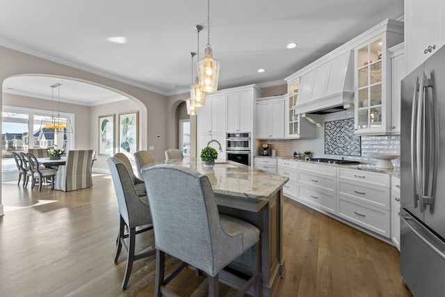 kitchen with a breakfast bar area, dark wood-type flooring, light stone countertops, custom exhaust hood, and stainless steel appliances