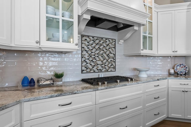 kitchen with tasteful backsplash, white cabinets, custom range hood, and glass insert cabinets