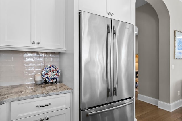 kitchen featuring white cabinets, arched walkways, decorative backsplash, and freestanding refrigerator