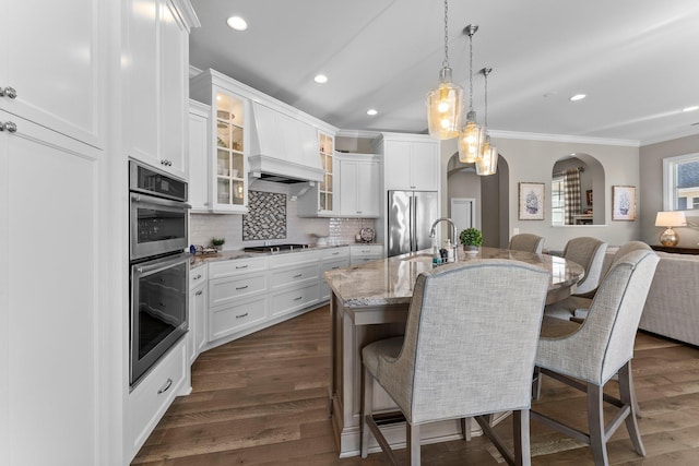 kitchen featuring arched walkways, appliances with stainless steel finishes, a kitchen breakfast bar, dark wood-style flooring, and backsplash