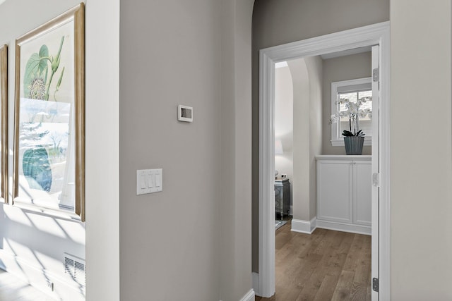 hallway featuring baseboards, arched walkways, and wood finished floors