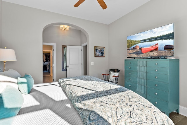 bedroom featuring arched walkways, a ceiling fan, wood finished floors, a walk in closet, and a closet