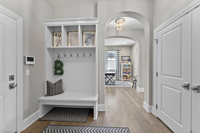 mudroom featuring arched walkways, baseboards, and wood finished floors